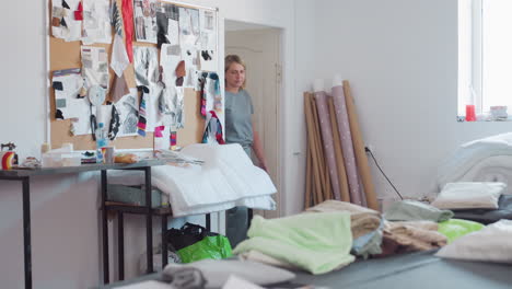 bright textile workshop filled with colorful fabric rolls, creative board covered in swatches, disposable cups on table, two creatives entering room, one picking paper before heading to worktable