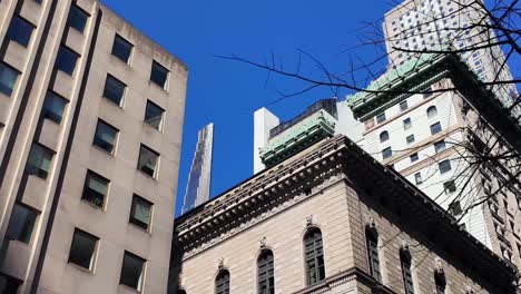 a low angle view, looking up at the tall skyscrapers in new york city from 5th avenue on a sunny day with clear blue skies