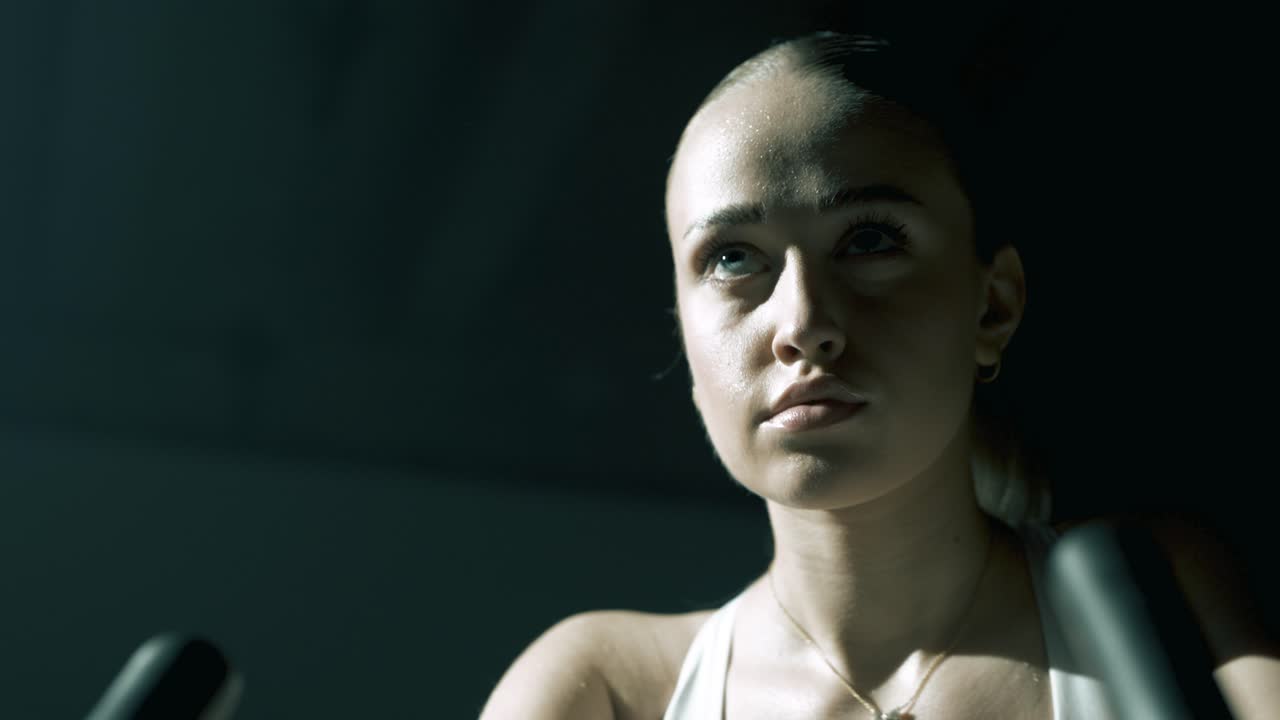 Low 45-degree angle shot moving from right to left, capturing a woman’s hand gripping the bike handlebar in foreground, with soft focus pulling onto her face in concentrated training expression