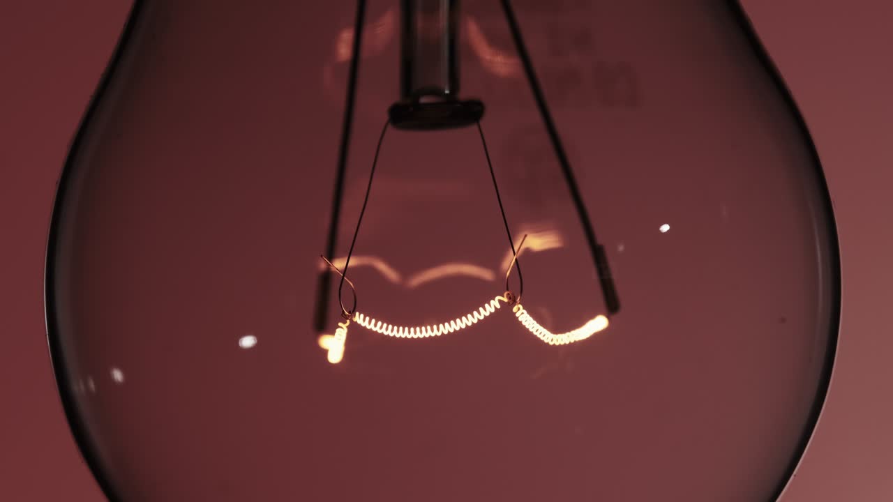 The Tungsten Filament in a Glass Lamp Close-up in Slow Motion on Red Background