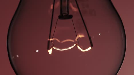 the tungsten filament in a glass lamp close-up in slow motion on red background