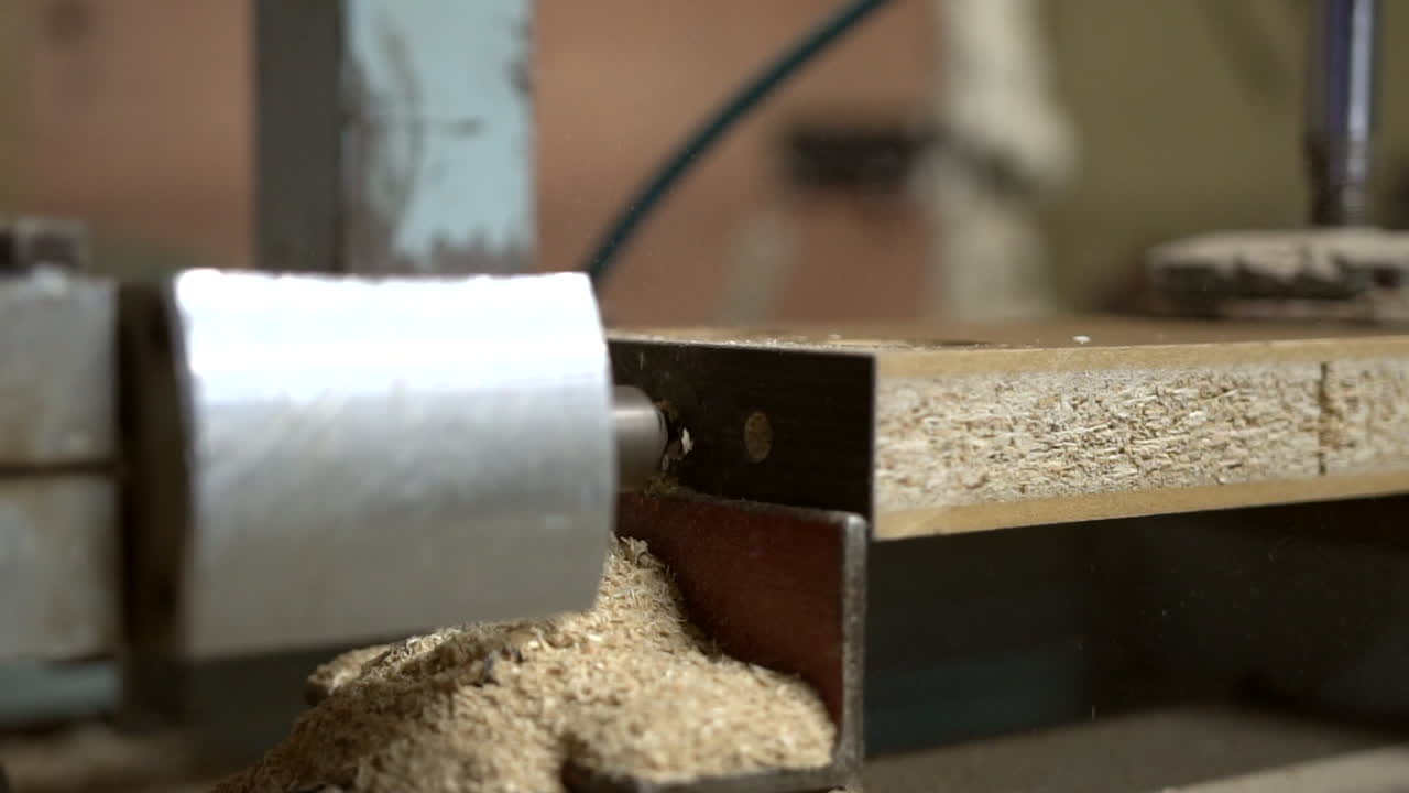 la broca técnica horizontal entra y sale en un elemento de madera aglomerada, produciendo mucho aserrín volador alrededor