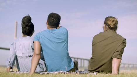 Back-view-of-people-sitting-on-meadow-and-pointing-at-horizon