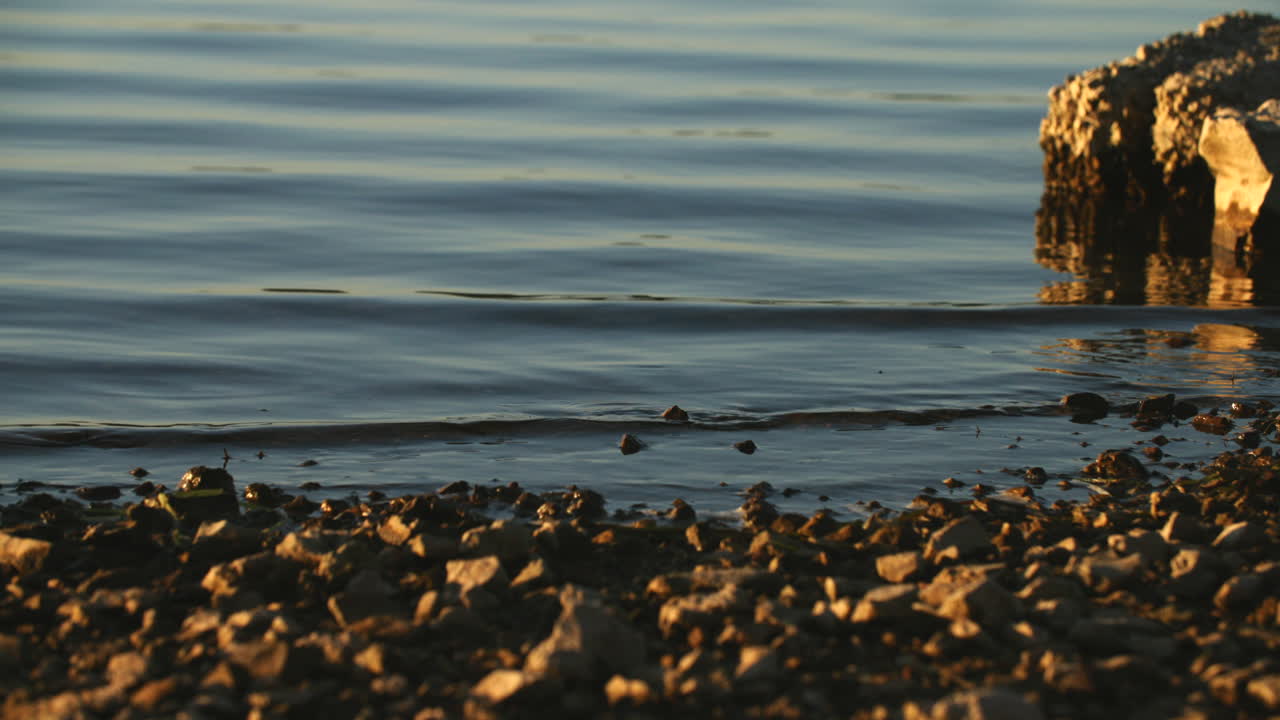 Slow motion footage of small waves moving up against the rocks on a beach during golden hour in Harrison, TN.