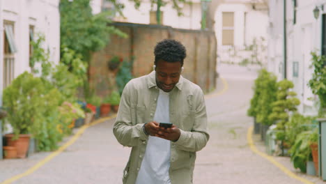 Young-Man-Travelling-Through-City-Listening-To-Music-On-Wireless-Earbuds-On-Mobile-Phone