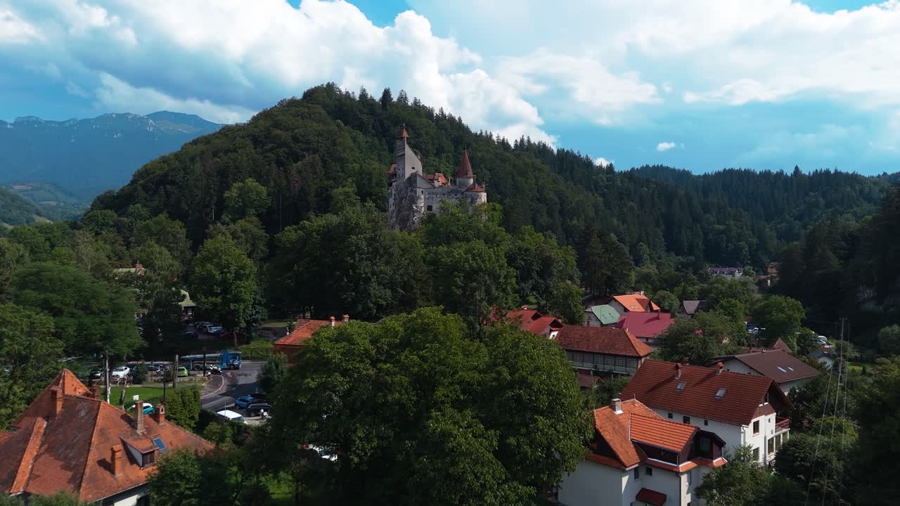 Volo veloce di drone che si alza verso il Castello di Bran sopra un villaggio boscoso.