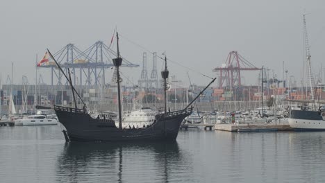 Ferdinand-Magellan-Nao-Victoria-Carrack-Bootsreplik-Mit-Spanischer-Flagge-Betritt-Den-Kai-In-Valencia-Mit-Containern-Und-Kränen-Im-Hintergrund-In-Zeitlupe-60-Fps