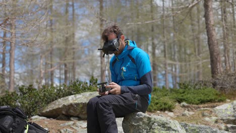 hombre con gafas de dron fpv sosteniendo un controlador sentado en una roca en el bosque