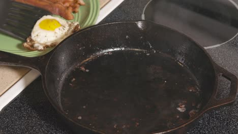 cast iron pan on stove frying egg and removing from pan