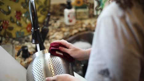 Over-the-Shoulder-shot-of-a-woman-washing-dishes-in-the-sink