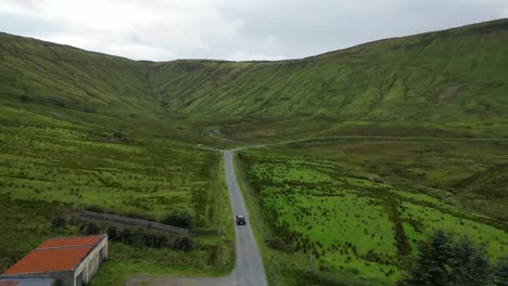 Drone-shot-of-a-car-driving-towards-Glenniff-Horseshoe,-flying-forwards-along-the-road