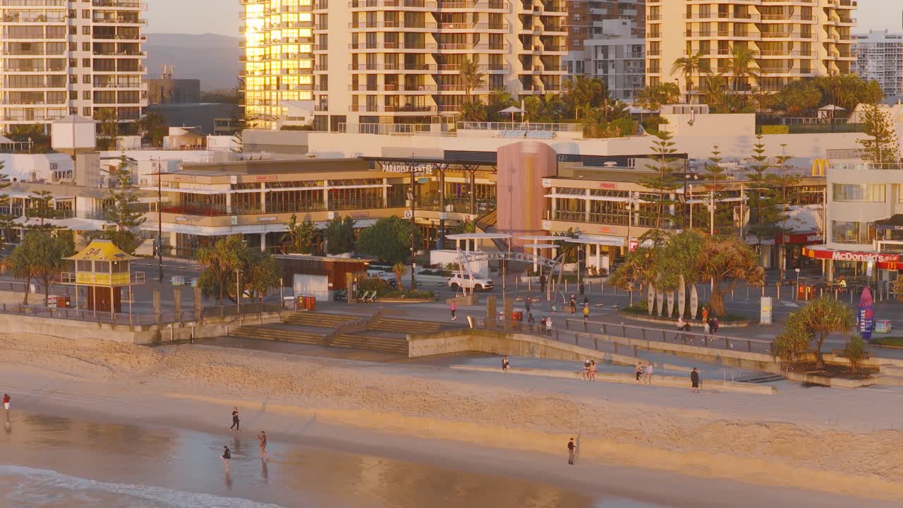 Aerial view of people walking along Gold Coast beach at sunrise, with cityscape backdrop and warm lighting