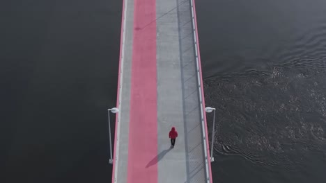 aerial view of a pink-striped bridge, person in red walking ahead, slow-motion