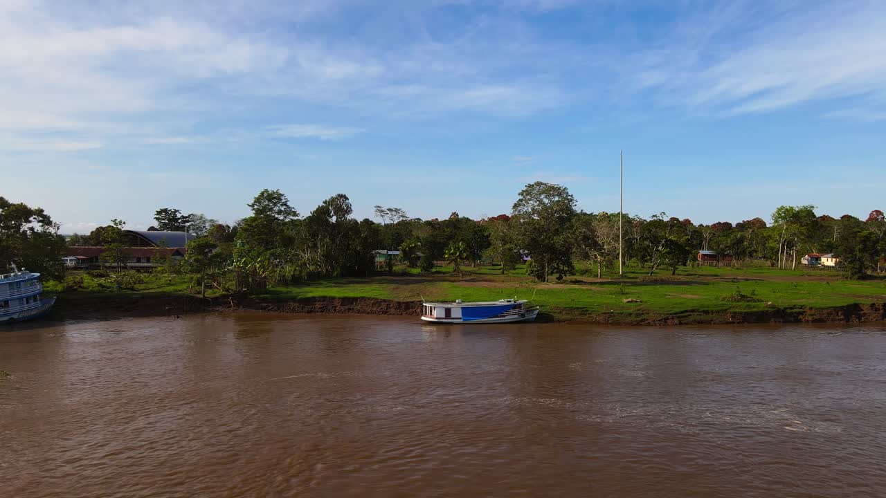 Boats on brown water by rural Brazilian Amazon landscape, aerial pan