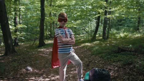 ginger caucasian boy wearing superhero costume standing with garbage bags.