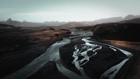 aerial thor valley, flying over glacial river flowing through black volcanic floodplain, mountains thorsmörk landscape iceland