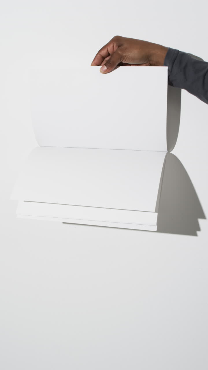 Vertical video of hand of african american man with book with white blank pages on white background