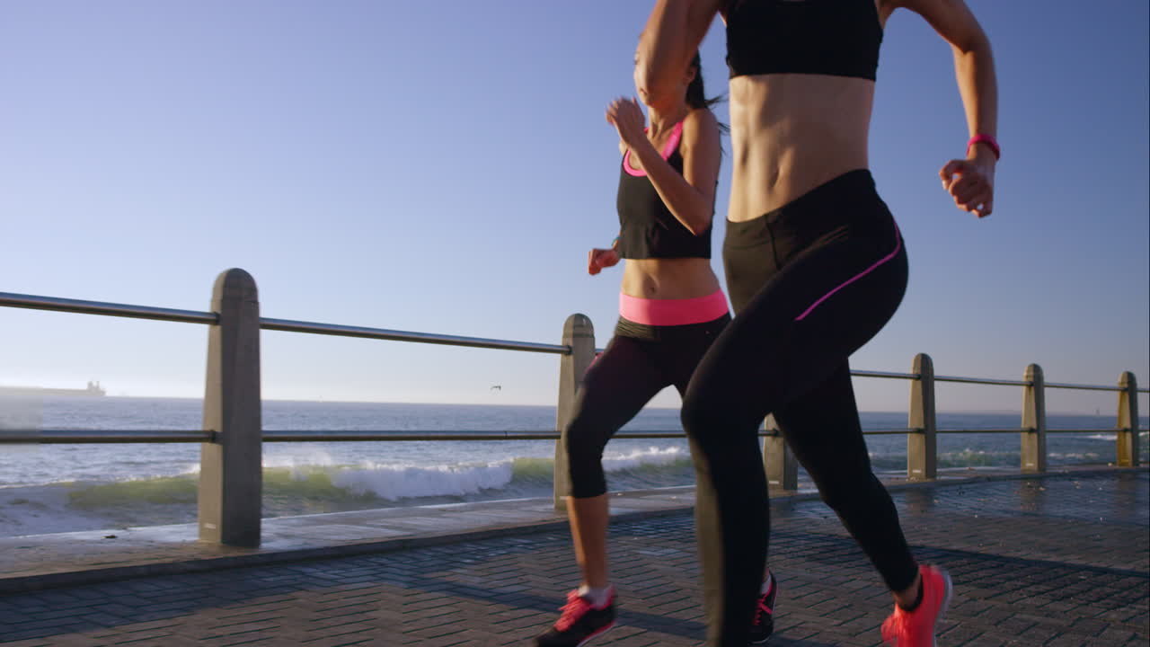dos mujeres atléticas corriendo al aire libre en cámara lenta en el paseo marítimo al atardecer cerca del océano disfrutando de la carrera nocturna
