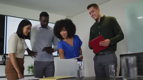 un groupe diversifié de collègues d'affaires en discussion dans une salle de réunion en utilisant un ordinateur portable et une tablette