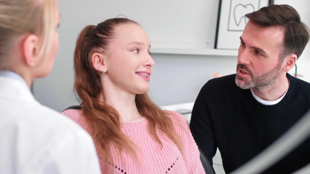 Dentist talking to teenage girl and her dad in dentist's clinic