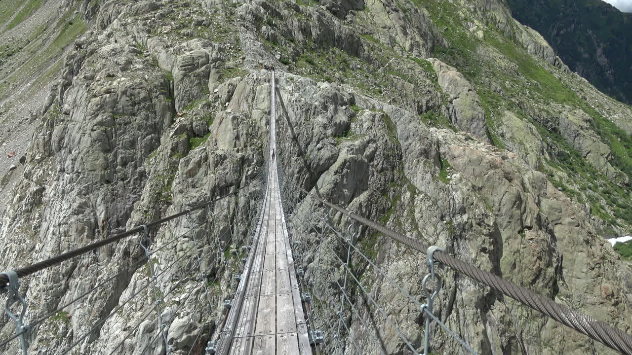 Vista aérea a lo largo del Puente Trift, un largo puente colgante peatonal que atraviesa un desfiladero alpino rocoso cerca de Gadmen, Oberland Bernés, Suiza, en un día soleado.