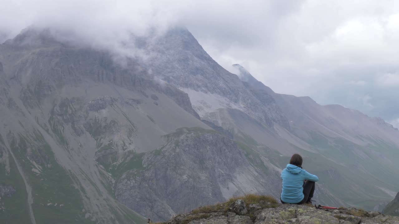 고독한 여성 등산객이 높은 고산 산과 계곡을 내다보고 있습니다.