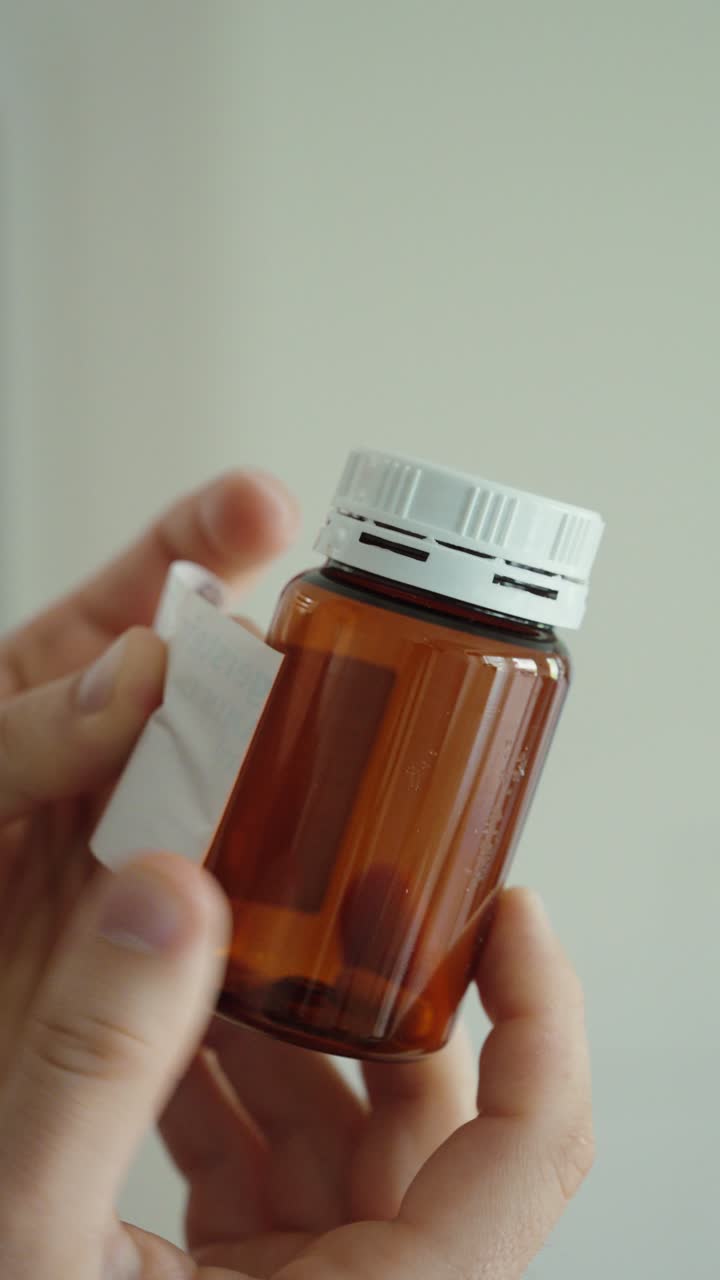 Primer plano de una mano despegando una etiqueta de un frasco de medicamento, representando el empaque, la manipulación del producto y el uso farmacéutico.