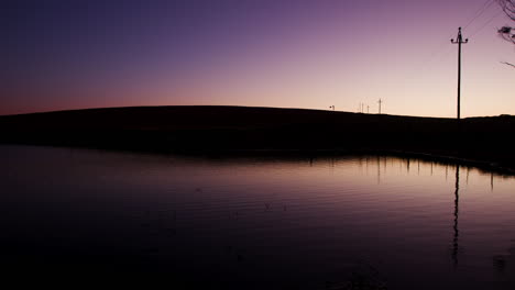 Dusk-or-dawn-static-shot-over-a-dam-on-a-still-day-reflecting-the-sky-on-the-surface-of-the-water