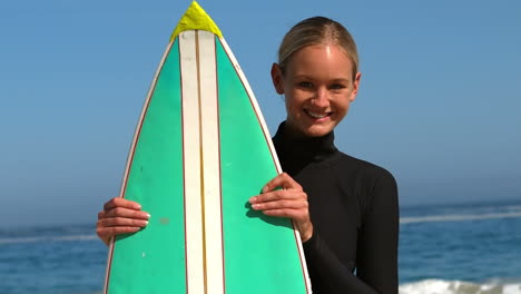 woman in wet suit hiding behind surfboard