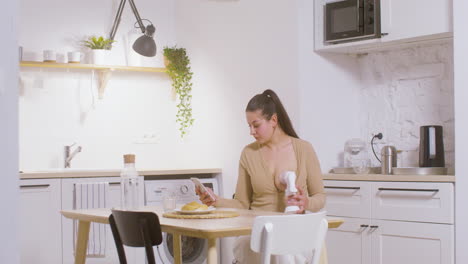 young mother using breast pump while sitting at table at home