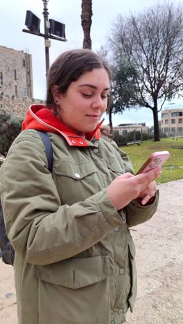 a woman wearing a green jacket and a red hoodie is holding a cell phone