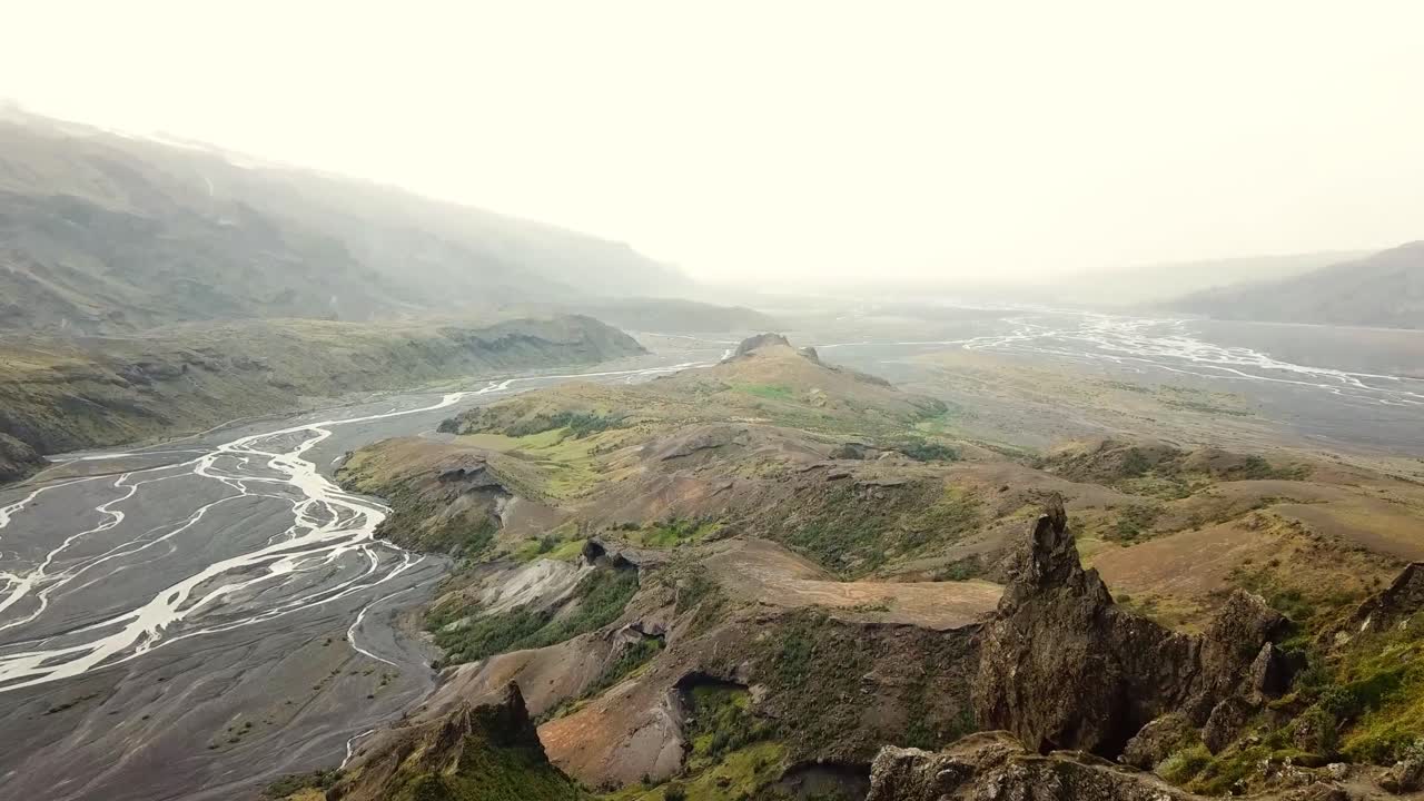 Breathtaking view of Þórsmörk, Iceland, highlighting a lush valley with braided rivers and moss-covered cliffs, surrounded by rolling hills and dramatic terrain under a soft, misty sky