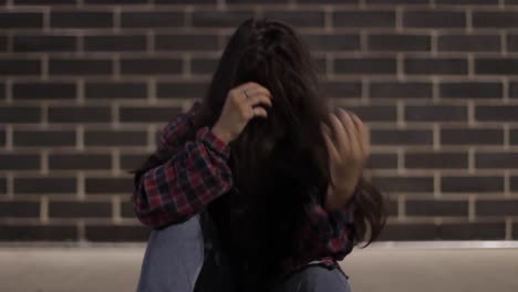 close-up shot of a woman sat down clearly upset and emotional with her face covered with her hair and hands