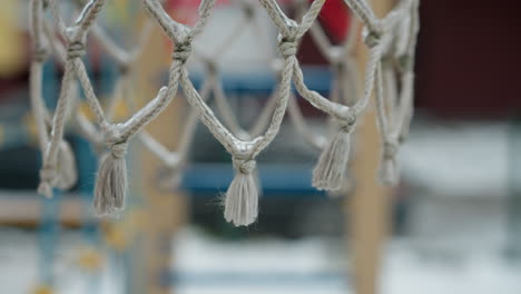 close-up of a frozen basketball net, emphasizing the icy fibers and knots against a blurred snowy playground backdrop, highlighting winter's chill effect on outdoor sports equipment