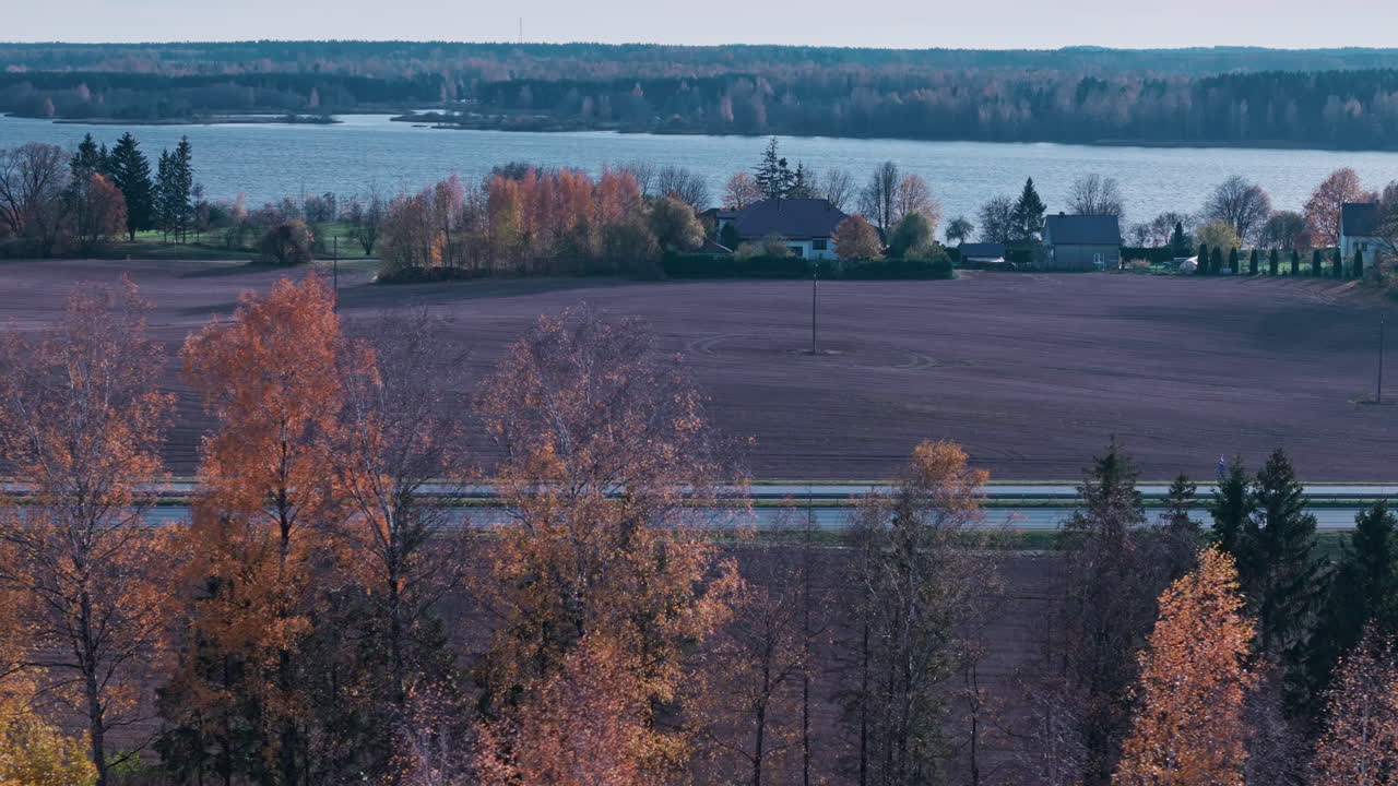 Bird's eye view of a countryside road with beautiful autumn-colored trees, houses, and a river in the background