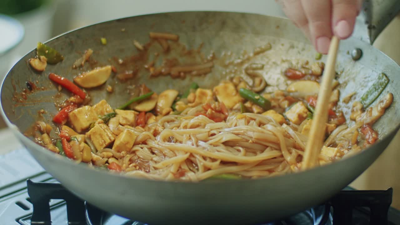 Woman mixing delicious wok noodles with chopsticks