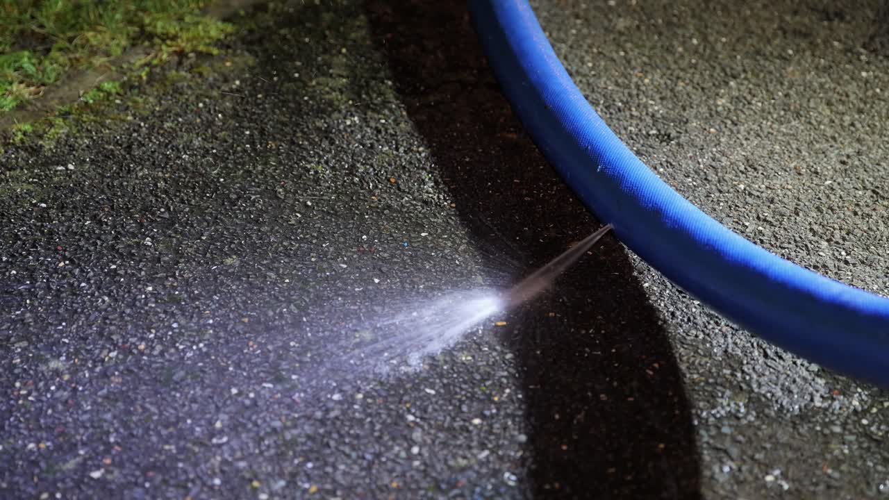 Getto d'acqua ad alta pressione spruzzato da un tubo flessibile sull'asfalto di notte