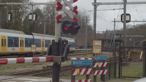 einfahrender zug in bahnhof mit geschlossenem bahnübergang im vordergrund