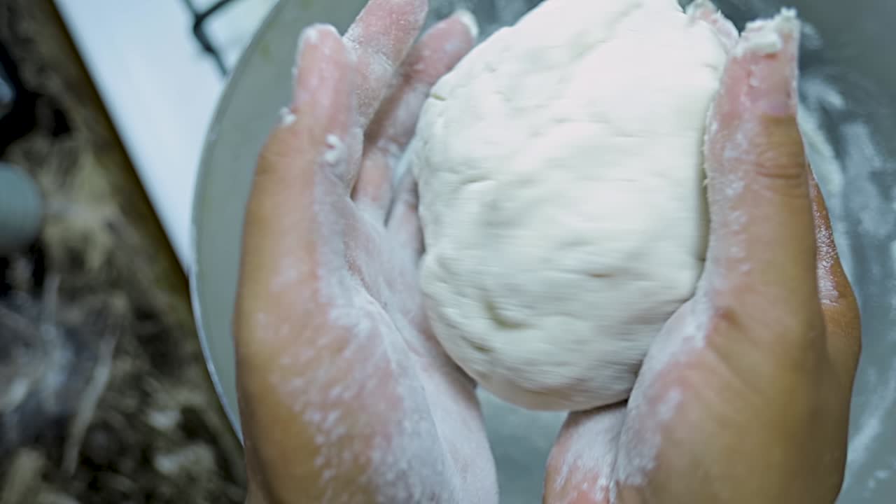close up view of African american woman's hands kneading pizza dough in a silver pan in slow motion