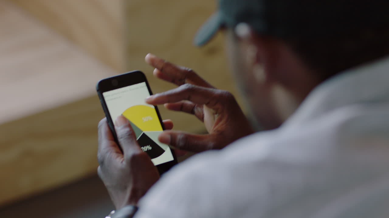 primer plano hombre de negocios afroamericano que usa un teléfono inteligente navegando datos de investigación en línea leyendo información de proyecto de mercado estudiante viendo estadísticas de desarrollo de empresas emergentes en la pantalla de su teléfono móvil