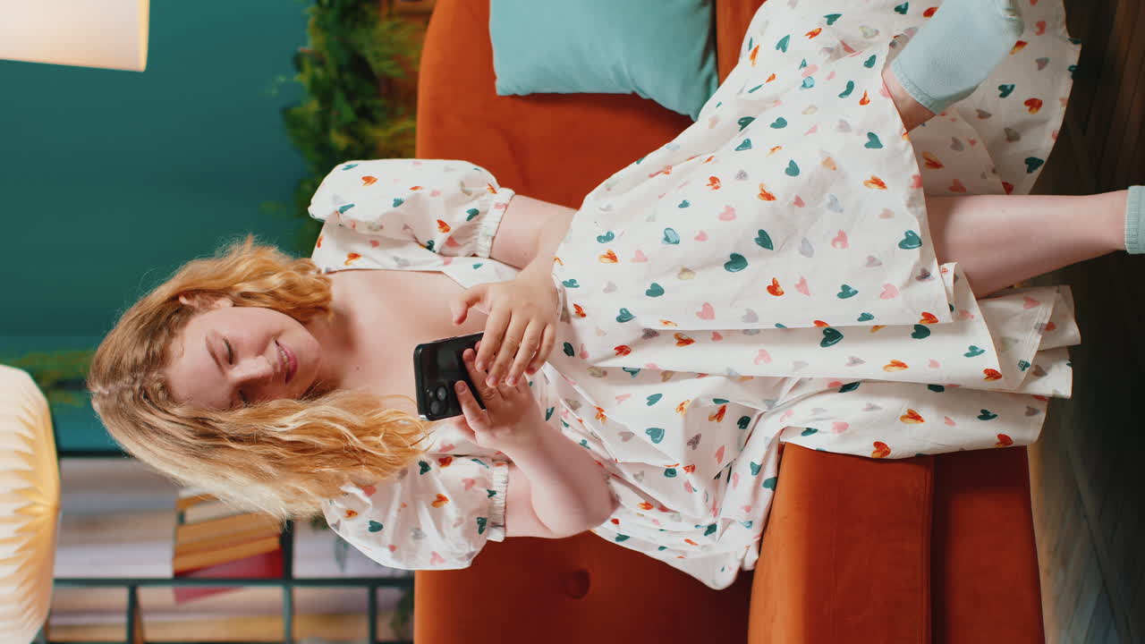 스마트폰을 사용하여 소파에 앉아있는 젊은 여성이 소셜 미디어 응용 프로그램에서 메시지를 공유합니다.