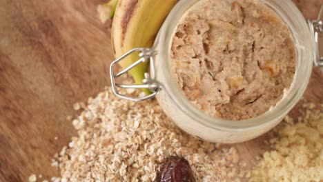 oatmeal porridge in jar next to bananas, dried dates on wooden background