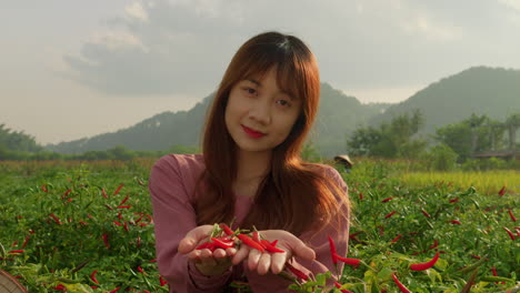 young-asiatic-woman-offering-red-hot-chili-pepper-in-front-of-camera-directly-from-organic-farm-plantation-while-smiling-in-slow-motion