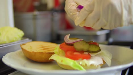 colocando cebollas en un bollo con verduras listas para hamburguesas en cámara lenta de comida rápida