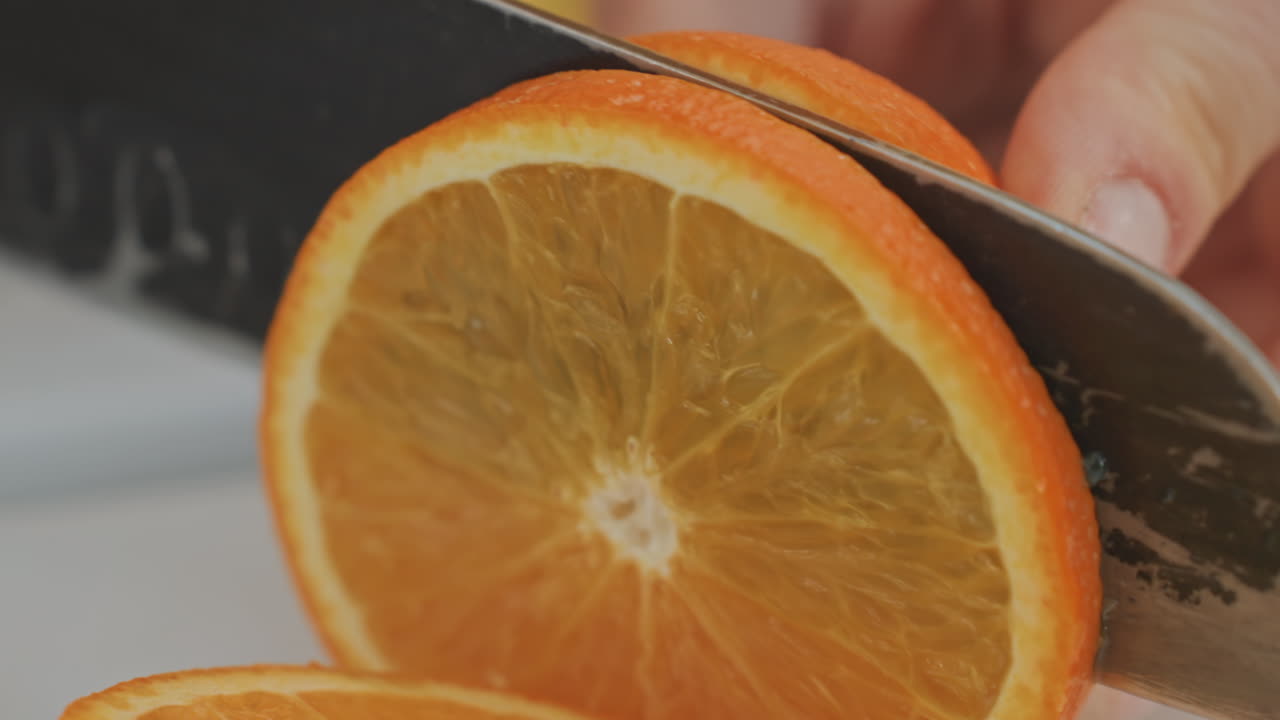 Primo piano di una fetta d'arancia tenuta in mano, un cuoco casalingo che affetta agrumi lucidi su un tagliere bianco, un coltello affilato che taglia la polpa, colore vibrante e consistenza succosa, atmosfera accogliente e luminosa in cucina, manicure visibile.