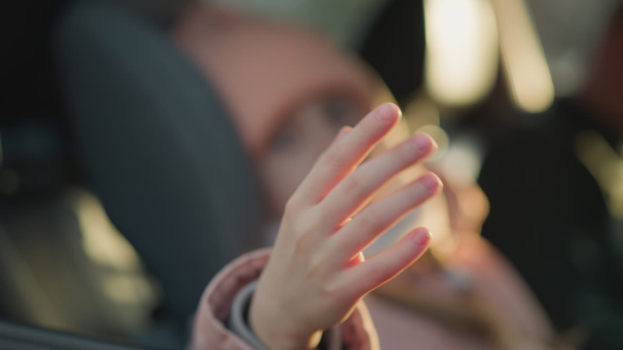 핑크색 재을 입은 어린 소녀가 손을 흔들고 있는 근접, 약간 초점 밖의 시선, 흐릿한 효과는 부드럽고 따뜻한 빛과 부드러운, 평화로운 분위기를 강조합니다.