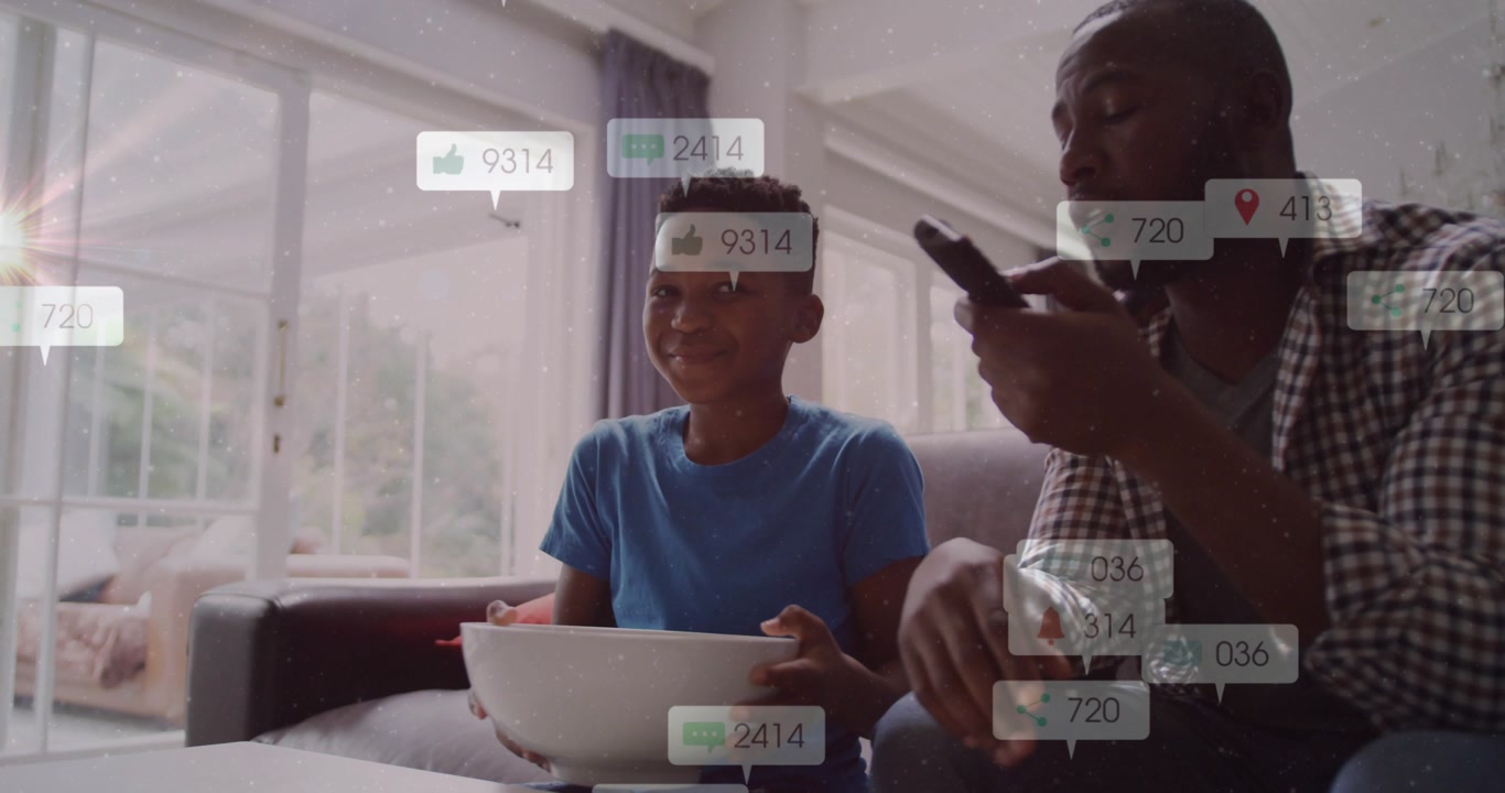 Father-son sitting on sofa boy pointing and causing social icons floating around bowl for marketers