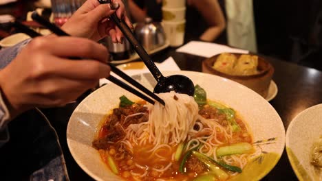 chopsticks lifting noodles from a soup bowl