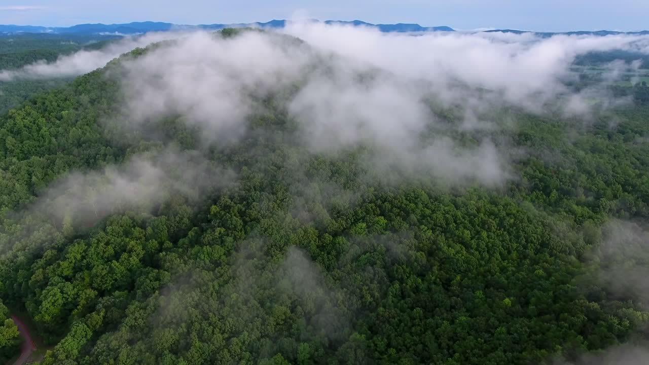 volando a través de nubes blancas bajas sobre el bosque verde de las grandes montañas humeantes