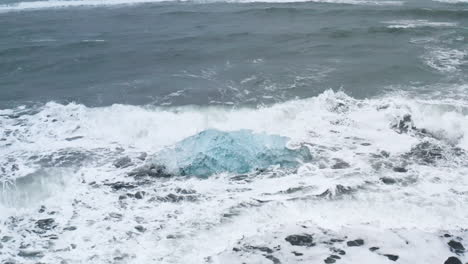 Stunning-drone-shot-of-waves-breaking-on-a-beautiful-ice-rock-at-Diamond-Beach-in-Iceland